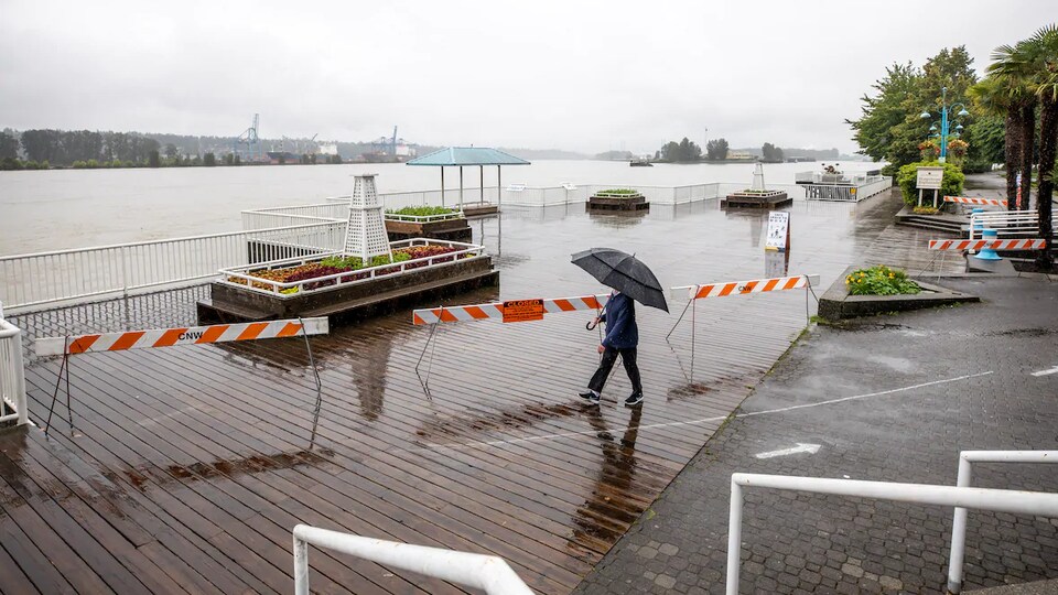 Une femme tenant un parapluie marche sur un secteur de la promenade en bois qui n'a pas été inondée à New Westminster, en Colombie-Britannique.