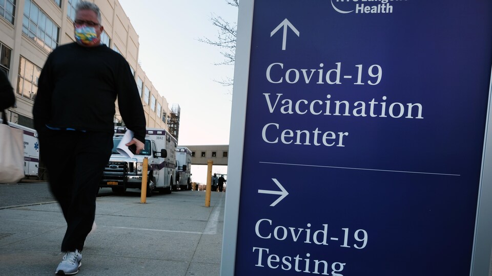 Des personnes passent devant un panneau indiquant une clinique de dépistage et un centre de vaccination.