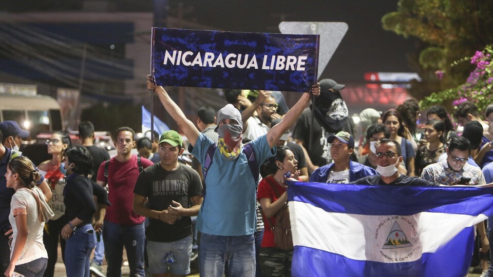 Un homme se tient devant des manifestants avec une affiche où on peut lire «Nicaragua Libre»