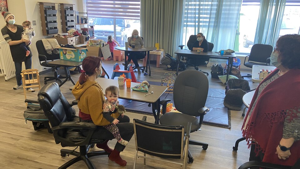 Des femmes avec leurs enfants dans une salle dotée de bureaux et de jouets.