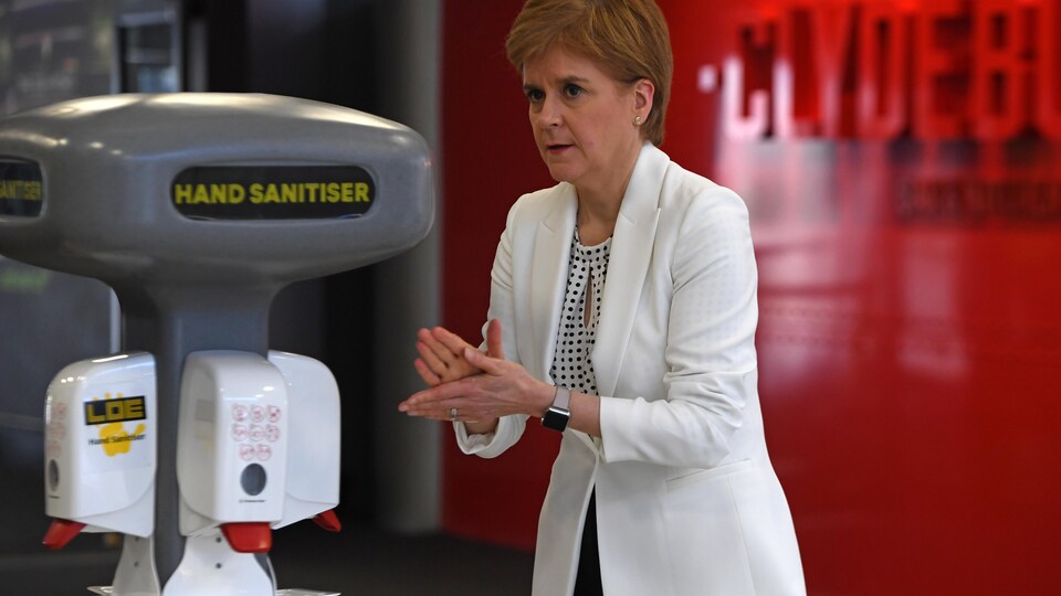 Nicola Sturgeon se frotte les mains devant une machine distribuant du gel désinfectant.