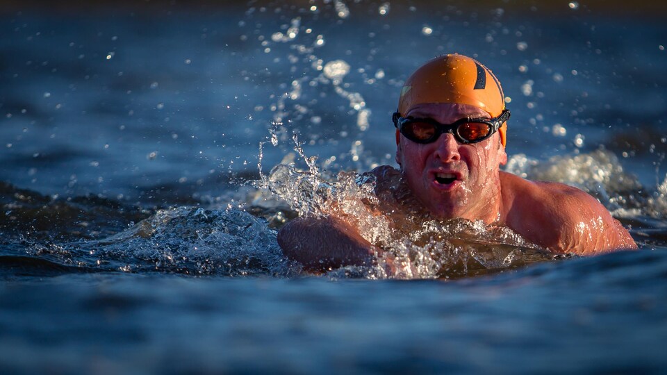 Un homme avec un bonnet de bain et des lunettes de nage en train de nager en eau ibre.