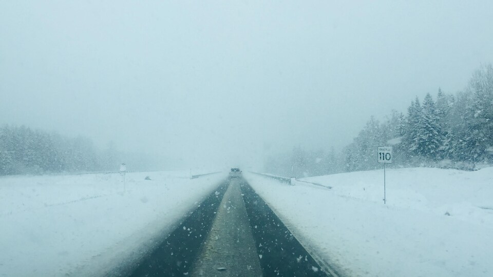 Une autoroute couverte de neige, à visibilité réduite.