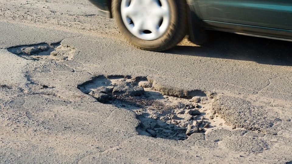 Une voiture évite un nid de poule.