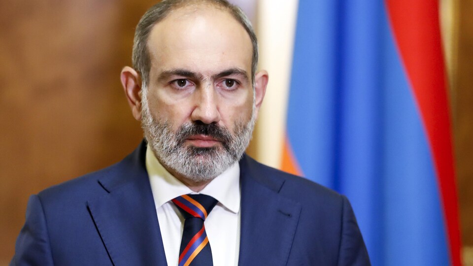 Gros plan de Nikol Pachinian, devant un drapeau arménien.