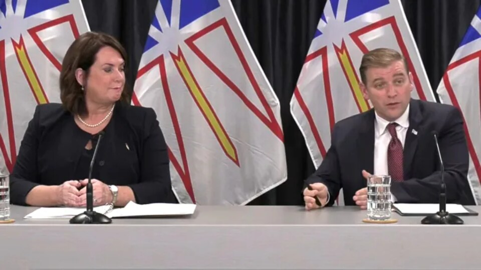 Siobhan Coady et Andrew Furey assis à une table, des drapeaux de Terre-Neuve-et-Labrador se trouvent derrière eux. 