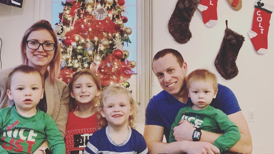 Patrick Burke est devant son sapin de Noël avec sa conjointe et ses enfants et ils sourient tous à la caméra.