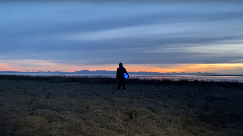 un homme devant un coucher de soleil et des montagnes