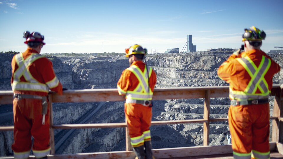 Trois ouvriers devant une mine à ciel ouvert.