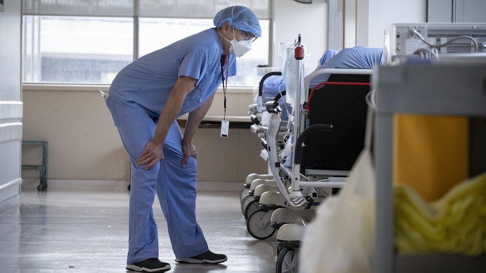Un travailleur de la santé discute avec un patient couchés sur une civière dans le couloir d'un hôpital.