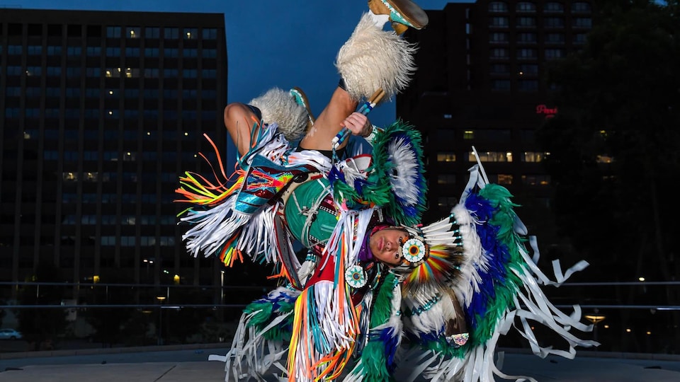 Notorious Cree, en habit traditionnel, fait une posture dans la rue de nuit.