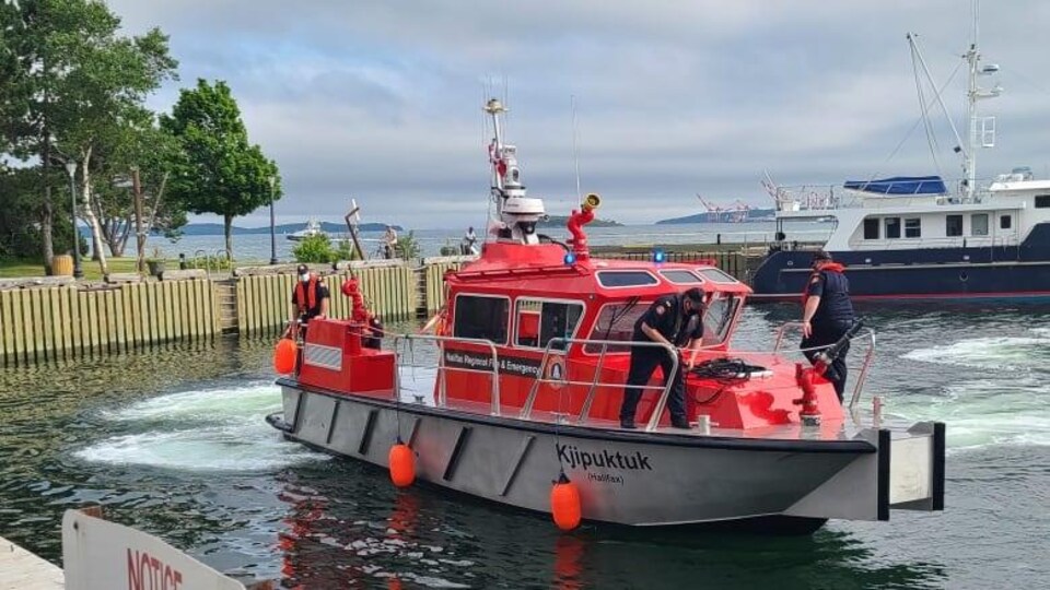 Deux pompiers sont sur le nouveau bateau rouge, sur lequel est écrit Kjipuktuk.