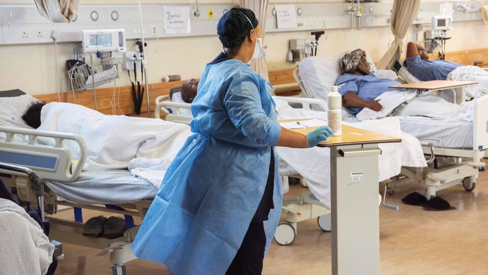 Une travailleuse de la santé passe entre des lits occupés dans un hôpital.