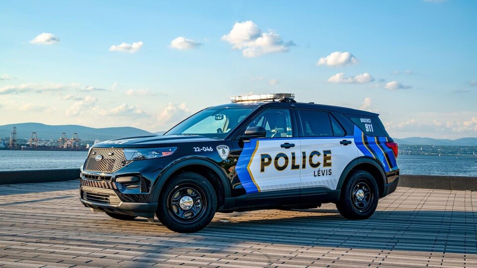 Une nouvelle voiture du Service de police de la Ville de Lévis, arborant le motif conçu par un patrouilleur. Le véhicule noir, bleu, doré et blanc est sur un quai en bordure du fleuve.