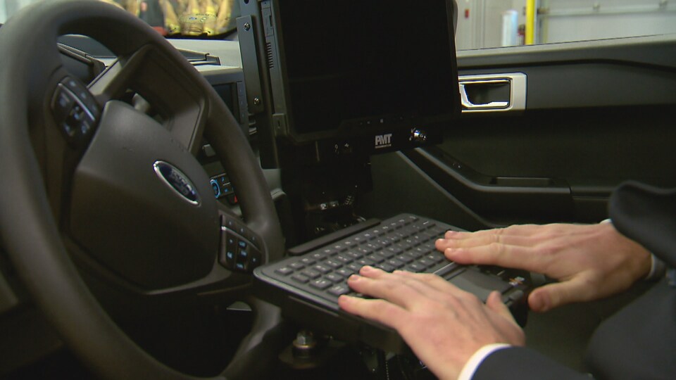 Un clavier d'ordinateur devant le volant d'une autopatrouille. Les mains d'un policier sont sur le clavier.