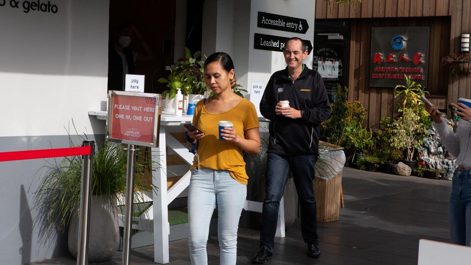 Une femme et un homme souriant marche, café en main. 