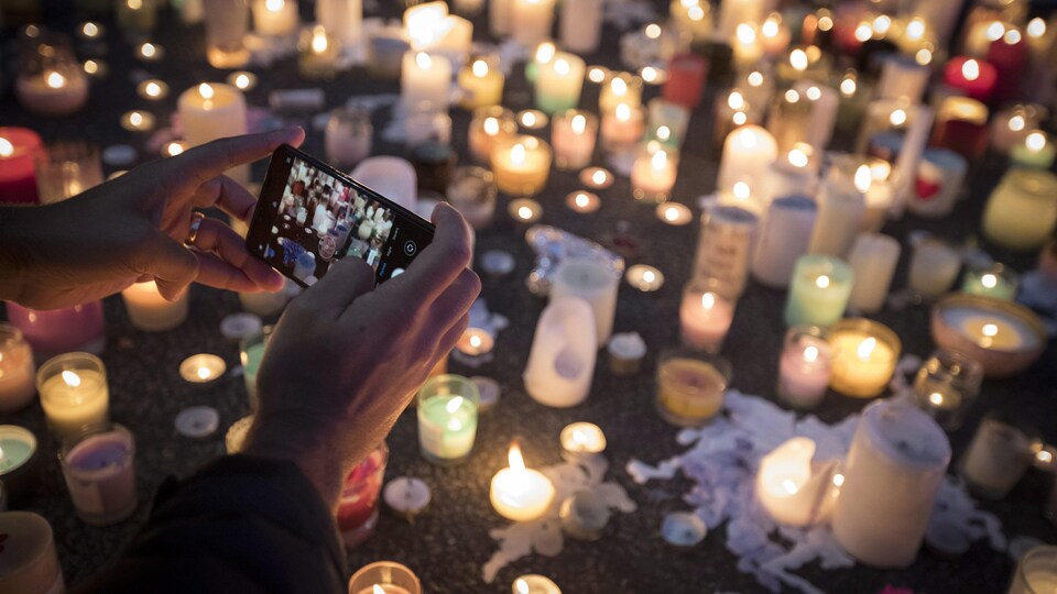 Une personne prend une photo avec son téléphone intelligent de nombreuses bougies allumées, en souvenir des victimes.