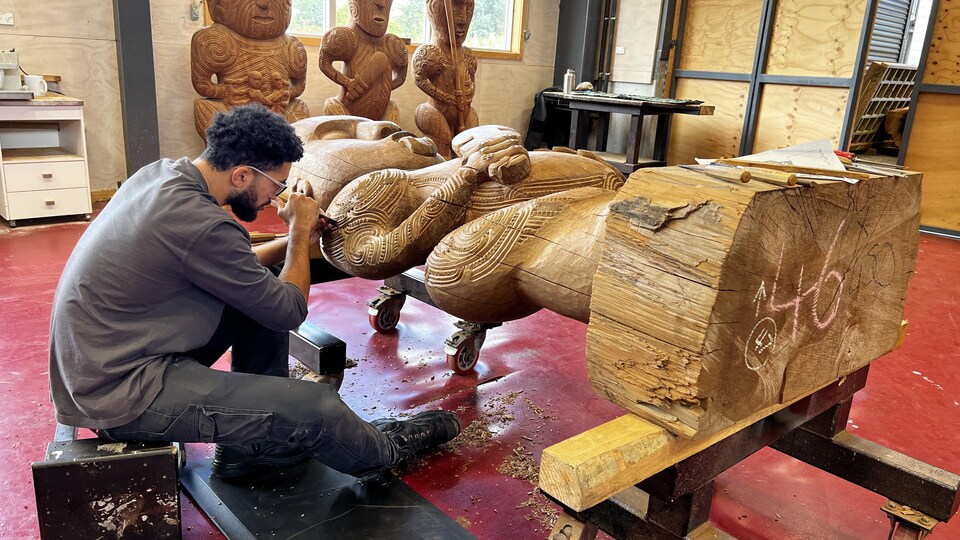 Un artisan travaille sur une grosse sculpture de bois. 