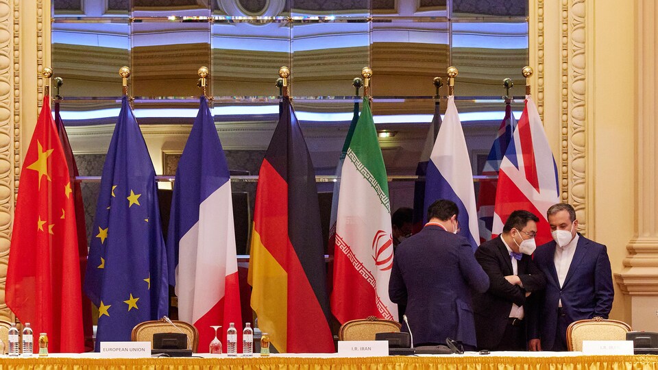 Trois hommes portant masque discutent debout devant une rangée de drapeaux.