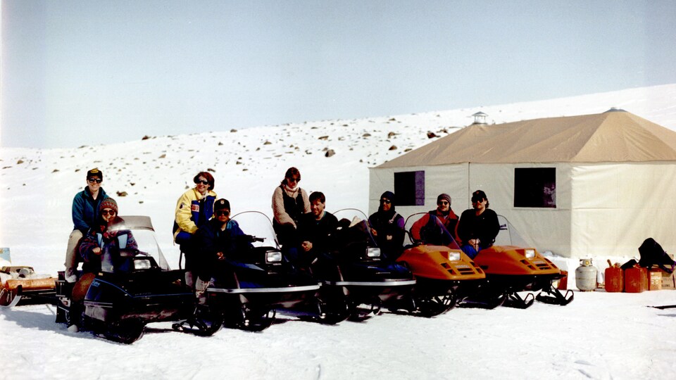 Neuf personnes sont assises derrière leur motoneige, au printemps 1993.