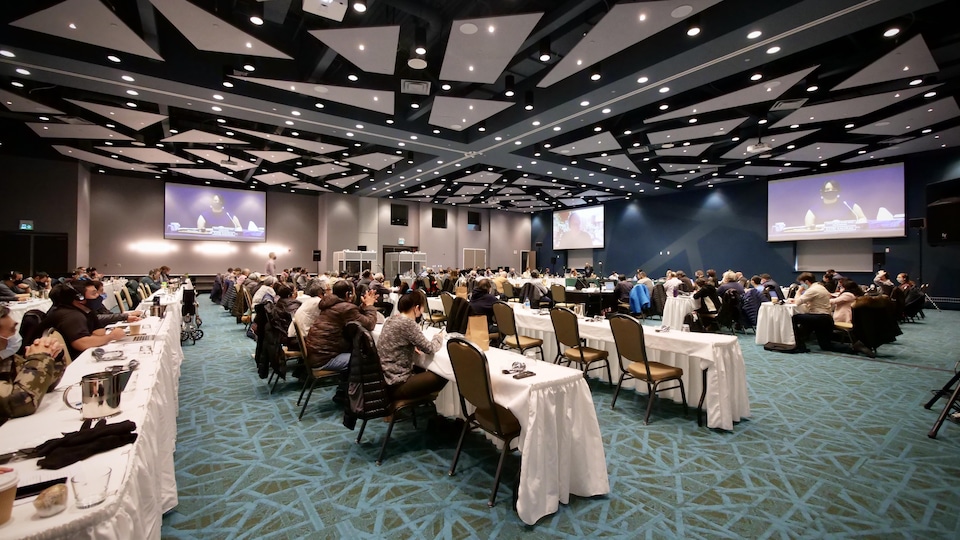 Des personnes sont assises dans une salle de conférence dans la cadre d'audiences publiques.
