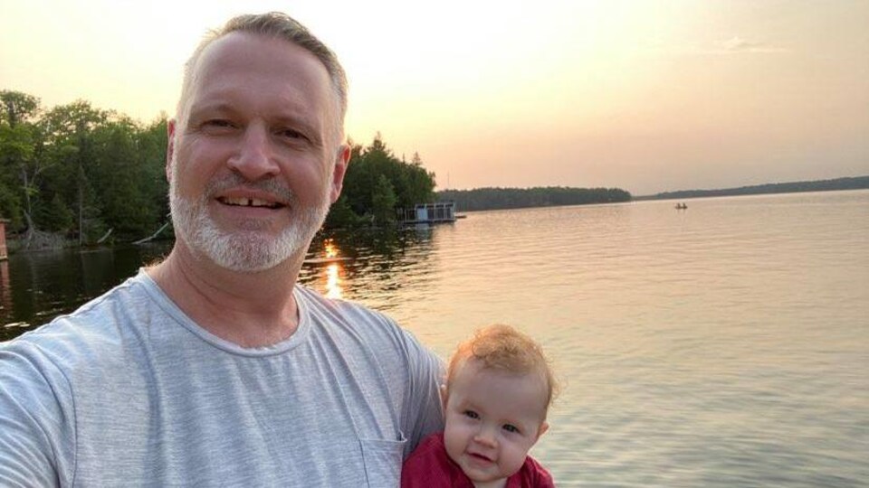 Égoportrait de Tim Brown devant un lac, sa fillette dans les bras.