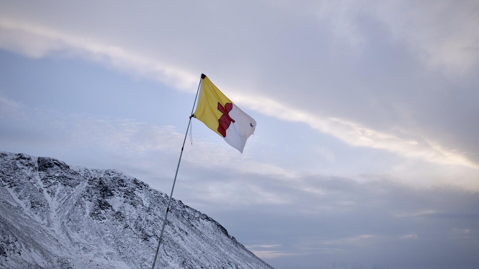 Un drapeau du Nunavut flotte dans le vent devant une montagne enneigée.