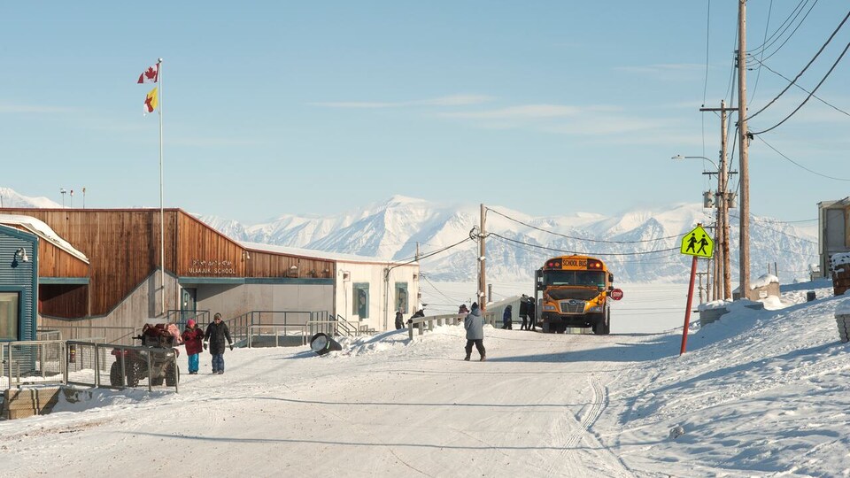 École et autobus scolaire en hiver, avec montagnes en arrière-plan, à Pond Inlet, au Nunavut, en 2019.