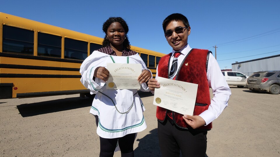 Deux élèves se tiennent devant un bus scolaire avec leurs diplômes
