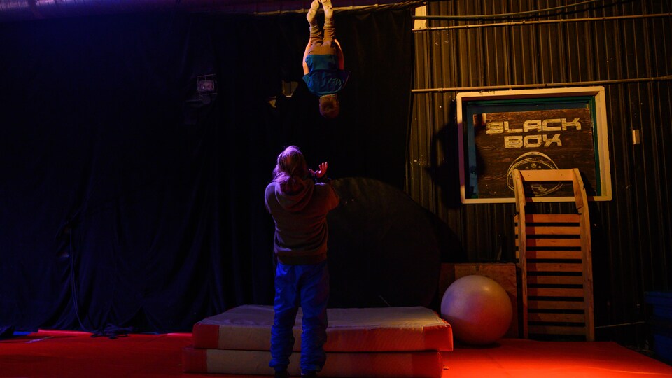 Un enfant effectue une culbute dans les airs pendant qu'un homme tend ses mains pour le rattraper.