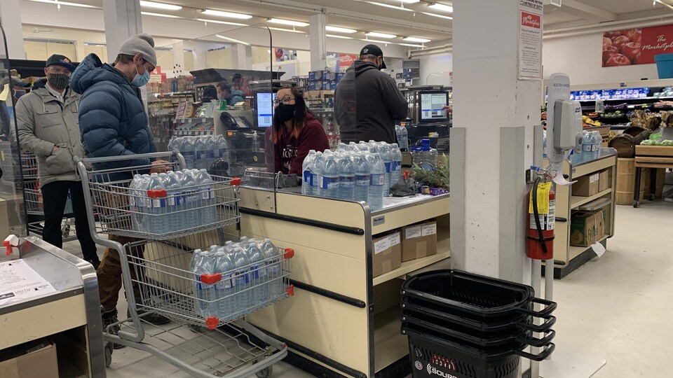 Des clients d'une épicerie achètent des bouteilles d'eau à la caisse.