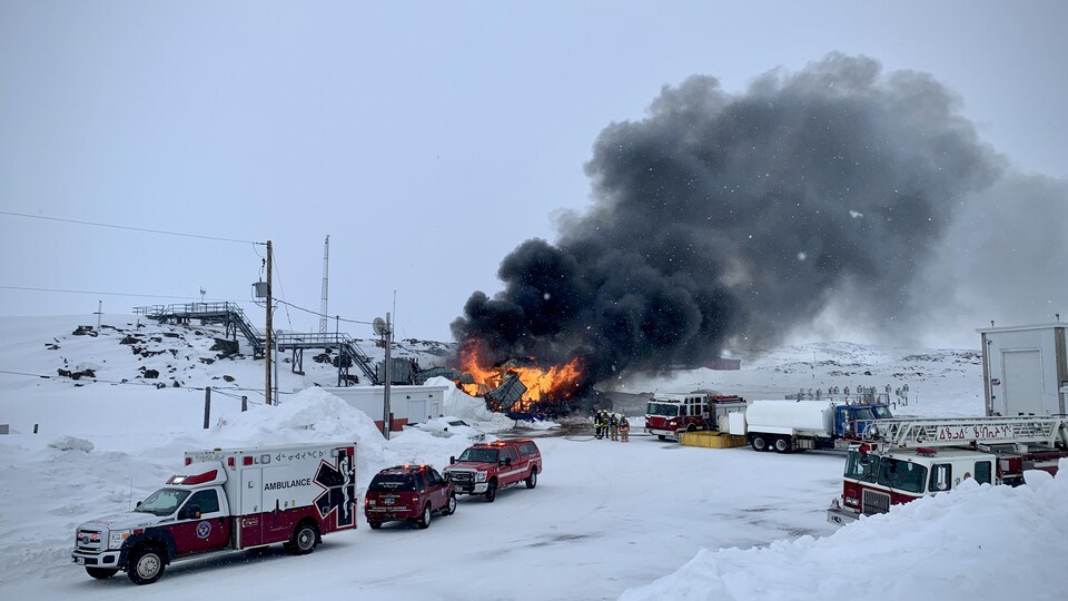 Des pompiers tentent d'éteindre l'incendie pendant que des flammes s'échappent du bâtiment.