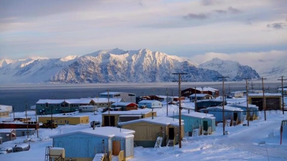 Un village enneigé devant une étendue d'eau et des montagnes.