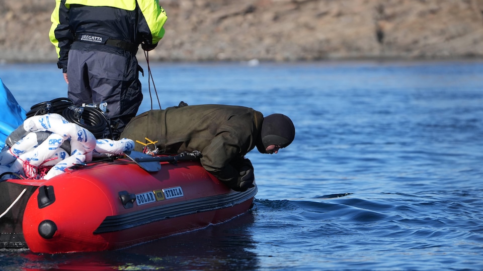 Une personne est debout dans un bateau de style zodiac et un plongeur est penché sur le rebord du bateau au Nunavut en août 2022.