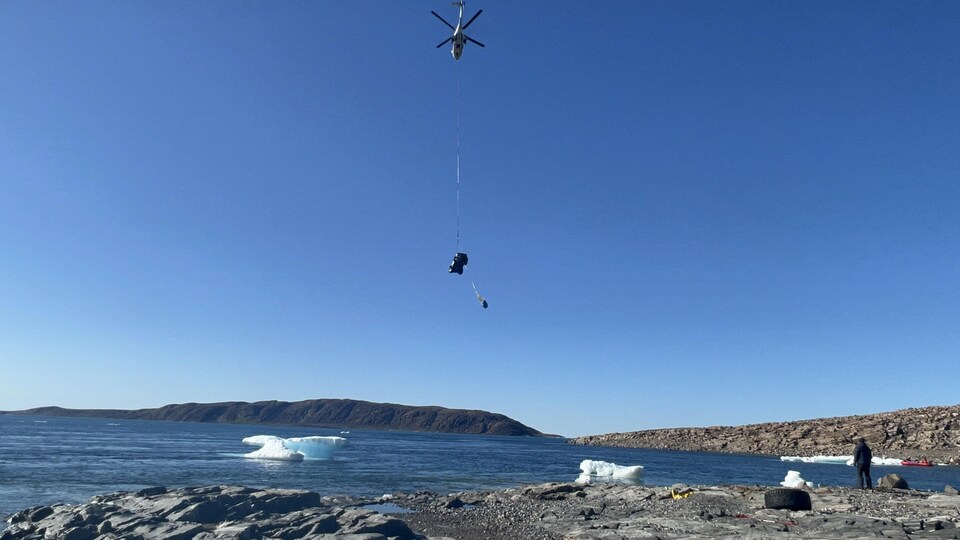 Un camion est soulevé par un câble attaché à un hélicoptère au-dessus de l'océan Arctique en août 2022.