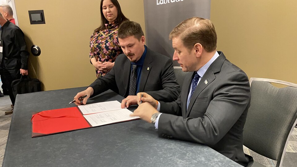 Le premier ministre du Nunavut, P.J. Akeeagok (à gauche) et celui de Terre-Neuve-et-Labrador, Andrew Furey (à droite), sont assis derrière une table et signent un document.