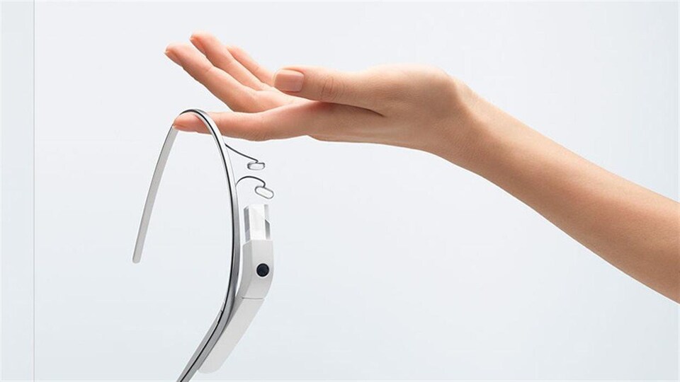 Une main tient au bout d'un doigt une paire de lunettes dotée d'un dispositif intelligent. 
