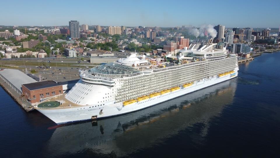 Photo aérienne d'un immense bateau de croisière, avec de hauts édifices du centre-ville d'Halifax derrière.