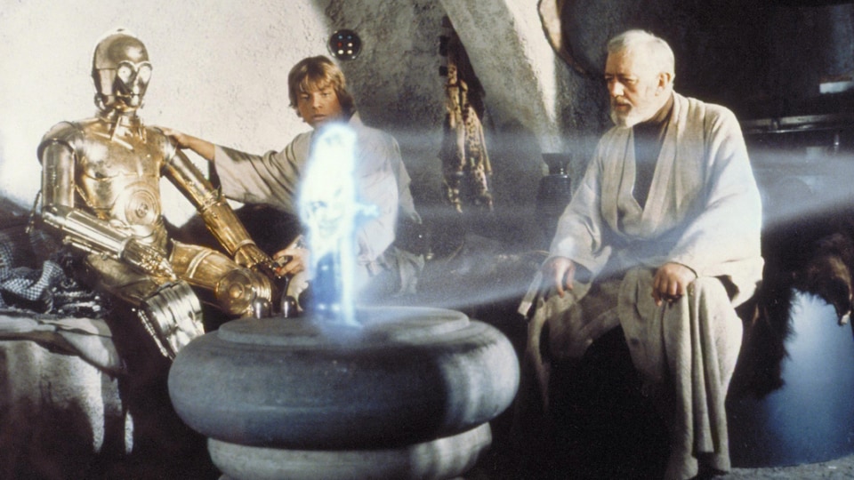 Un robot, un hologramme et deux chevaliers jedi dans une scène du film star wars. 