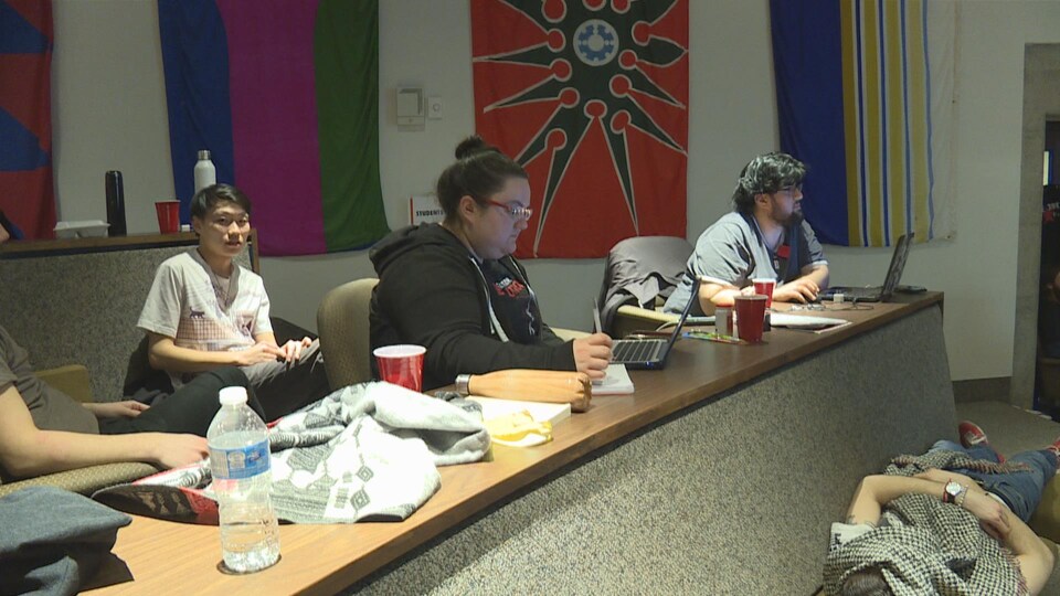 Photo d'étudiants à une table et d'un autre couché au sol.