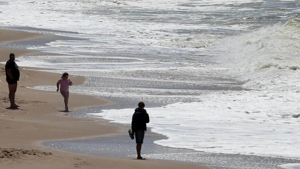 Des gens marchent dans le sable sur le bord de l'océan Atlantique. 