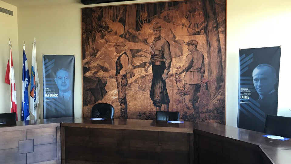La peinture géante qui illustre trois personnages sur le bord d'une rivière est installée dans la salle du conseil municipal de Baie-Comeau.