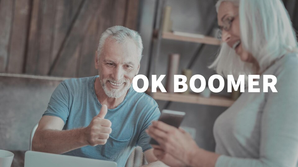 Un homme âgé fait un pouce en l'air devant un téléphone intelligent tenu par une femme. Le titre OK Boomer est par-dessus la photo.
