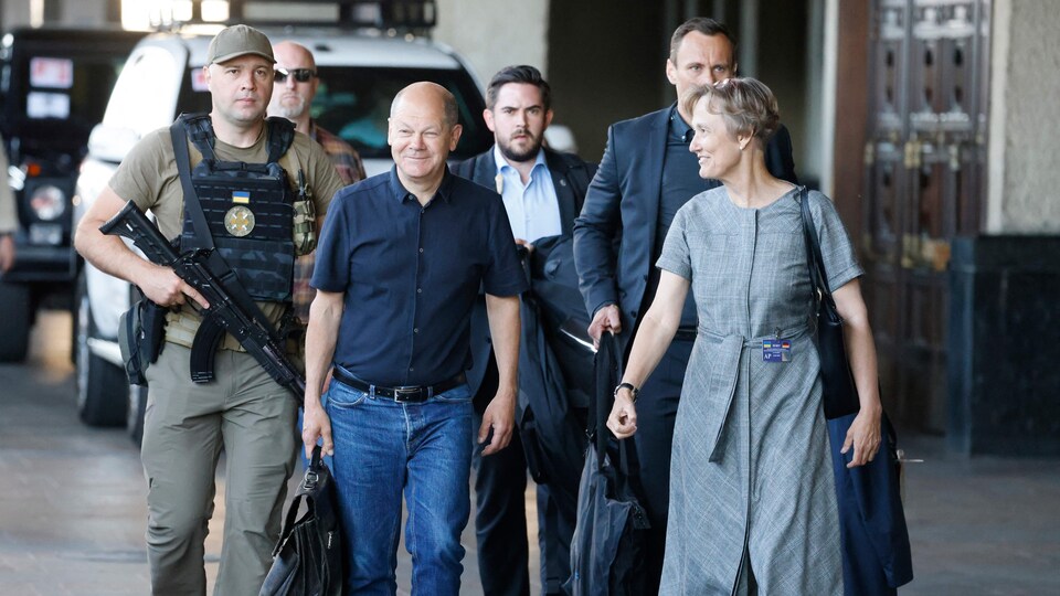 Olaf Scholz et une femme marchent escortés par des hommes armés.