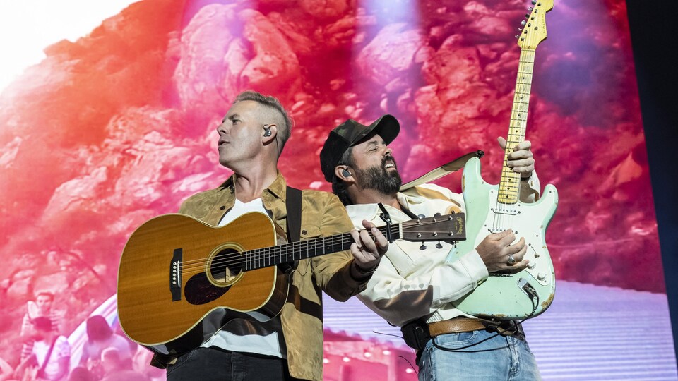 Deux musiciens dos à dos tiennent des guitares pendant un spectacle.