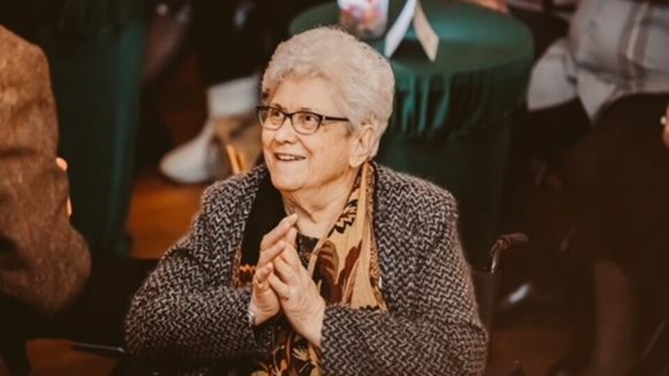 Olga Lapuk est assise et regarde en souriant un homme debout vu de dos.