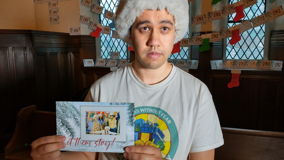 Omar Chu, qui milite au sein du groupe de défense des migrants Sanctuary Health, tient un carte de Noël déclarant, «Permettez-leur de rester! »