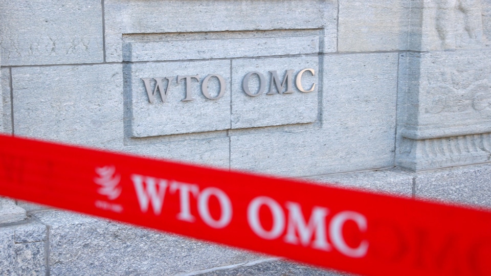 L'édifice de l'Organisation mondiale du commerce avec un plan rapproché de l'inscription « O M C » sur un mur de pierre.