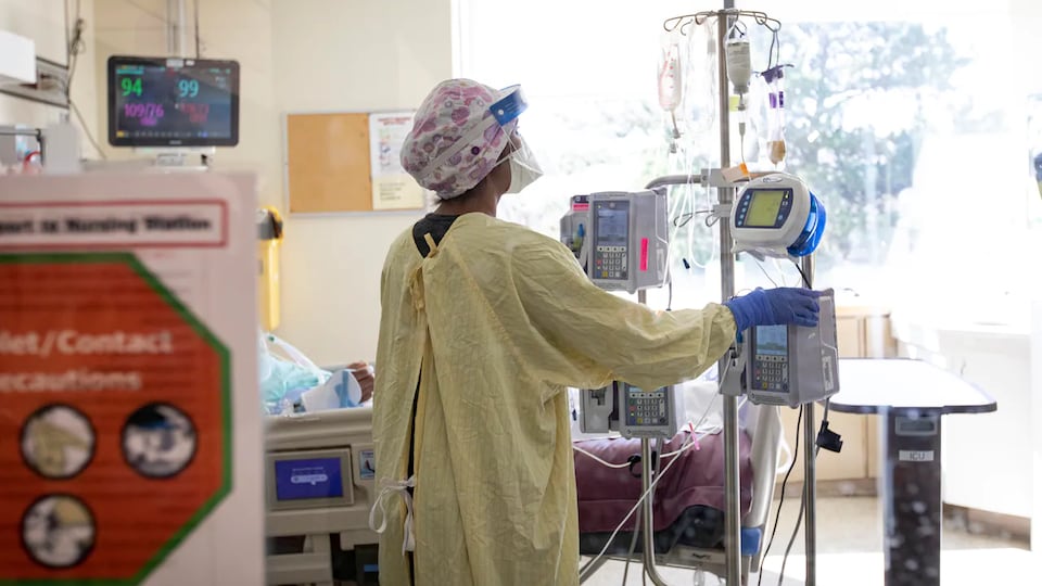Un membre du personnel consulte de l'équipement médical tout près du lit d'un patient dans une chambre d'hôpital.
