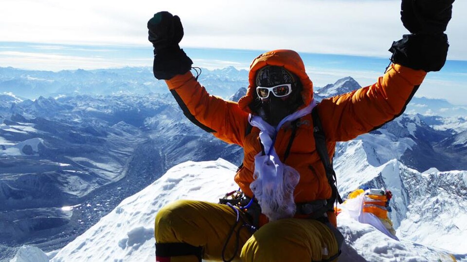 une personne levant les bras au sommet de l'Everest.